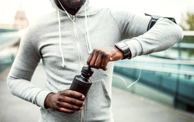 A close-up of unrecognizable young sporty black man runner with water bottle in a city. - HPIF30105