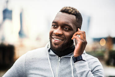 Young sporty black man runner with smartphone standing in a city, making a phone call. A close-up. - HPIF30120