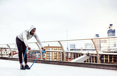 Junger aktiver schwarzer Sportler beim Training mit elastischen Gummibändern auf einer Brücke in London. - HPIF30130