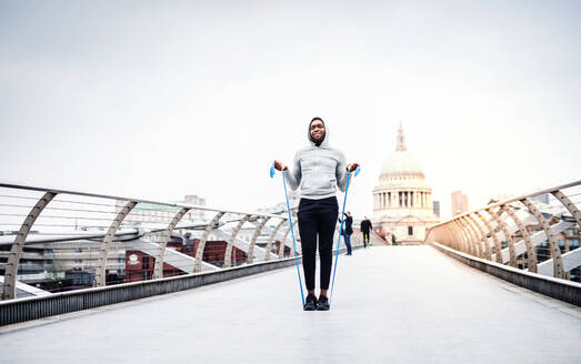 Junger aktiver schwarzer Sportler, der mit elastischen Gummibändern auf einer Brücke in London trainiert, im Hintergrund die St. Paul's Cathedral. - HPIF30131