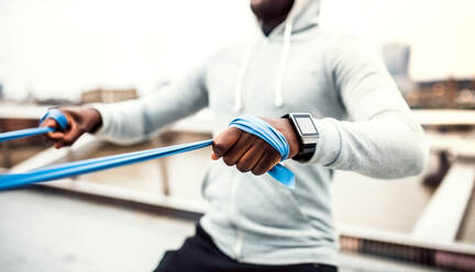 Unbekannter junger aktiver schwarzer Sportler, der auf einer Brücke in London mit elastischen Gummibändern trainiert. - HPIF30136