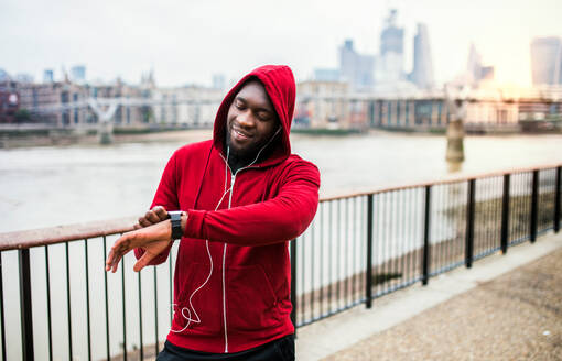 Junge sportliche schwarze Mann Läufer Einstellung Smartwatch auf der Brücke außerhalb in einer Stadt. - HPIF30147