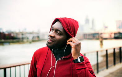 Nahaufnahme eines schwarzen Läufers mit Smartwatch, Kopfhörern und Kapuze auf dem Kopf, der in einer Stadt steht. Raum kopieren. - HPIF30148