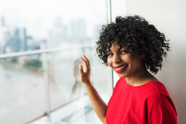 A portrait of woman standing by the window against London rooftop view panorama. Copy space. - HPIF30158