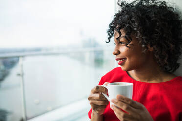 A close-up of a woman standing by the window holding a cup of coffee. Copy space. - HPIF30162