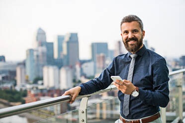 Porträt eines Geschäftsmannes mit Smartphone, der vor dem Panorama eines Londoner Daches steht, Kopierraum. - HPIF30195