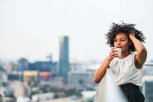 A close-up portrait of a black woman standing on a terrace, drinking coffee. Copy space. - HPIF30212