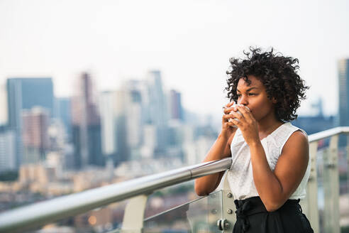 A portrait of a black woman standing on a terrace, drinking coffee. Copy space. - HPIF30213