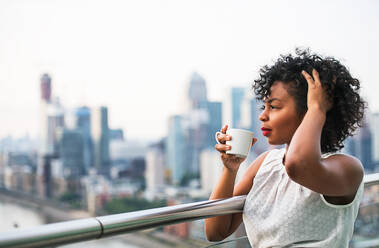 Nahaufnahme eines Porträts einer schwarzen Frau, die auf einer Terrasse steht und Kaffee trinkt. Kopierraum. - HPIF30215