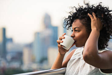 Nahaufnahme eines Porträts einer schwarzen Frau, die auf einer Terrasse steht und Kaffee trinkt. Kopierraum. - HPIF30216