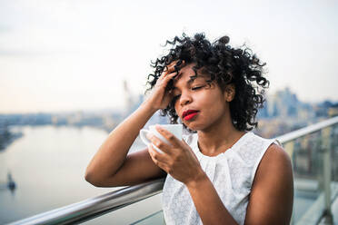 A close-up portrait of a black woman standing on a terrace, drinking coffee. Copy space. - HPIF30217