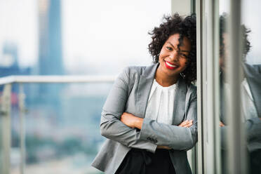 A portrait of black businesswoman standing on a terrace against London rooftop view panorama, arms crossed. Copy space. - HPIF30231