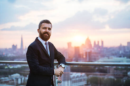 Porträt eines Geschäftsmannes mit Jacke vor dem Panorama eines Londoner Daches bei Sonnenuntergang. Kopierraum. - HPIF30254