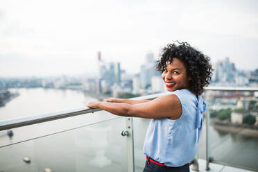 Porträt einer lachenden schwarzen Frau, die auf einer Terrasse in London steht und sich an einem Geländer festhält; Kopierraum. - HPIF30267