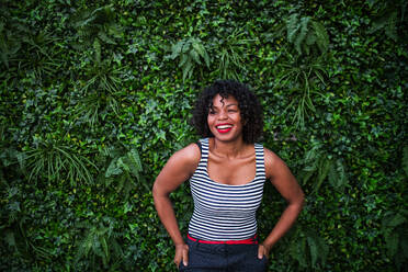 Ein Porträt einer schwarzen lachenden Frau vor einem grünen Hintergrund aus Buschblättern. - HPIF30272