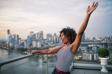 Ein Porträt einer schwarzen Geschäftsfrau, die vor dem Panorama einer Londoner Dachterrasse steht und ihre Begeisterung zum Ausdruck bringt. Raum kopieren. - HPIF30283