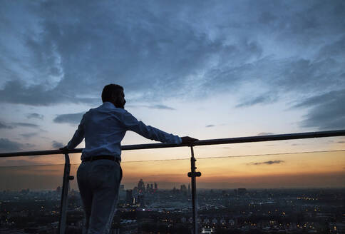 Rückansicht eines Hipster-Geschäftsmannes, der in der Abenddämmerung vor dem Panorama Londons steht. Raum kopieren. - HPIF30285