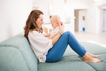 Young mother with a baby boy at home sitting on the sofa, playing. - HPIF30307