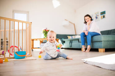 Ein kleiner Junge, der zu Hause auf dem Boden spielt, mit einer nicht erkennbaren Mutter auf dem Sofa im Hintergrund. - HPIF30309
