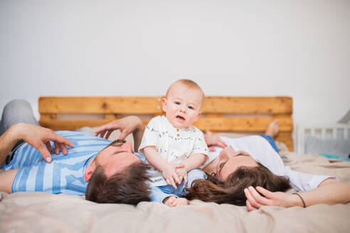 Glückliche junge Familie mit einem kleinen Jungen zu Hause, auf dem Bett liegend. - HPIF30316