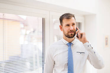 A young man in white shirt, and tie with a smartphone inside in the office, making a phone call. Copy space. - HPIF30323
