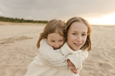 Happy girl giving piggyback ride to sister at beach - VIVF00983