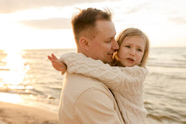 Lächelnder Vater umarmt Tochter bei Sonnenuntergang - VIVF01003