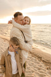 Vater, der seine Tochter umarmt, mit einem am Strand stehenden Jungen - VIVF01004