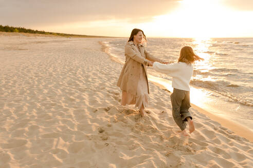 Happy mother and daughter having fun on coastline at sunset - VIVF01013