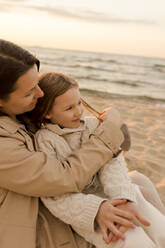 Smiling mother embracing daughter at beach - VIVF01021