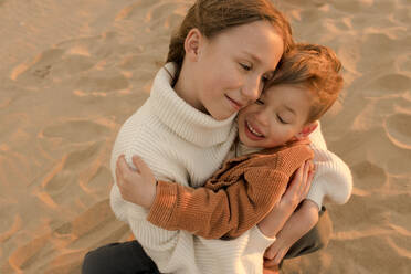 Smiling sister hugging brother at beach - VIVF01022