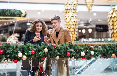 Ein glückliches junges Paar mit Smartphone in einem Einkaufszentrum zur Weihnachtszeit, Textnachrichten. - HPIF30331