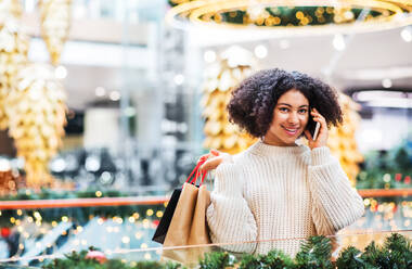 Porträt eines Teenagers mit Smartphone und Papiertüten in einem Einkaufszentrum zu Weihnachten, der einen Anruf tätigt, Kopierraum. - HPIF30334