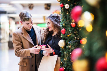 Ein glücklicher junger Mann, der seiner Freundin in einem Einkaufszentrum zur Weihnachtszeit ein Geschenk überreicht. Kopierraum. - HPIF30339