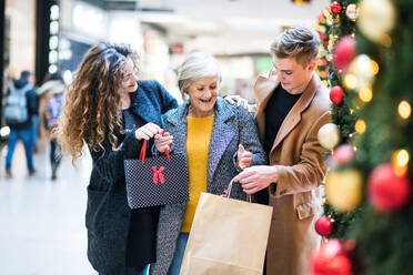 Ein Porträt der älteren Großmutter und der Enkelkinder im Teenageralter mit Papiertüten, die in einem Einkaufszentrum zur Weihnachtszeit stehen. - HPIF30340