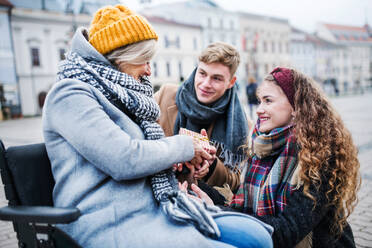 Zwei glückliche Teenager schenken einer behinderten Großmutter im Rollstuhl ein Geschenk im Freien im Winter. - HPIF30341