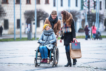 Teenagerpaar und ältere Großmutter im Rollstuhl gehen im Winter die Straße hinunter. - HPIF30342