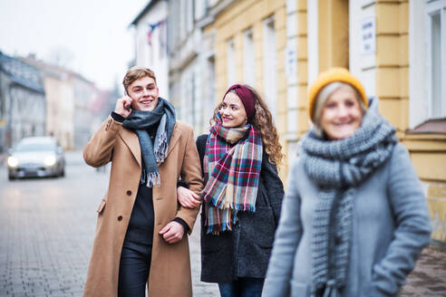 Großmutter und Enkelkinder im Teenageralter gehen im Winter auf der Straße spazieren. Ein Junge mit Smartphone führt ein Telefongespräch. - HPIF30347