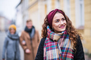 A portrait of teenage girl with headband and scarf standing on the street in winter. Christmas shopping concept. - HPIF30348