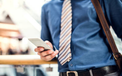 Ein unerkannter junger Geschäftsmann mit Smartphone geht in einem modernen Gebäude spazieren und schreibt eine SMS. - HPIF30363