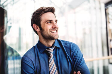 A portrait of a happy young businessman standing inside a building, arms crossed. - HPIF30373