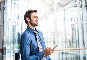 A young businessman with smartphone standing in a modern building, text messaging. Copy space. - HPIF30376