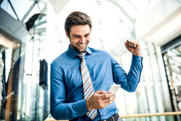 Ein junger Geschäftsmann schaut auf sein Smartphone und freut sich über eine gute Nachricht. - HPIF30377