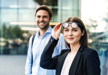 A waist-up portrait of young businessman and businesswoman with glasses standing outdoors. - HPIF30390