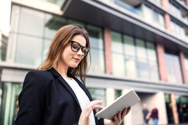 A young businesswoman using tablet outdoors in front of a building in a city. Copy space. - HPIF30396