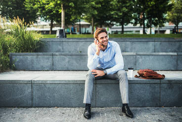 Ein Geschäftsmann mit Smartwatch und Kopfhörern, der im Freien auf einer Betontreppe sitzt. - HPIF30404