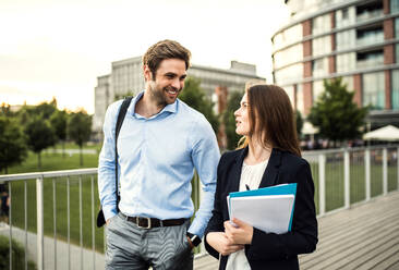 A young businessman and businesswoman walking on a bridge, talking. - HPIF30410