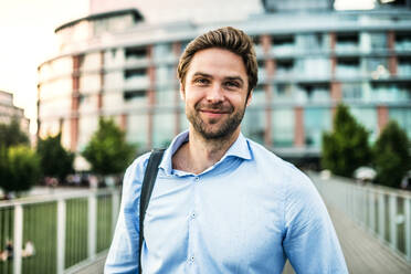 A portrait of a handsome young businessman with a bag walking on a bridge. - HPIF30411