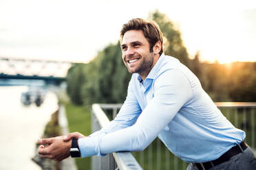 Ein junger Geschäftsmann, der auf einer Brücke steht und sich auf ein Geländer stützt. Raum kopieren. - HPIF30415