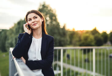 A young businesswoman with smartphone outdoors, making a phone call. Copy space. - HPIF30423